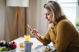 Giovane donna seduta al tavolo all'interno di casa, usando lo smartphone quando si rilassa.
