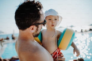 Un padre con un bambino piccolo con bracciali in piedi in piscina durante le vacanze estive.