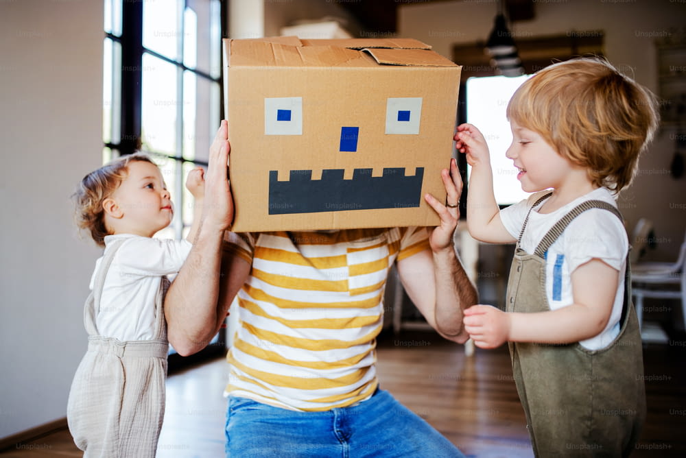 Two happy toddler children with a father and cardboard monster playing indoors at home.