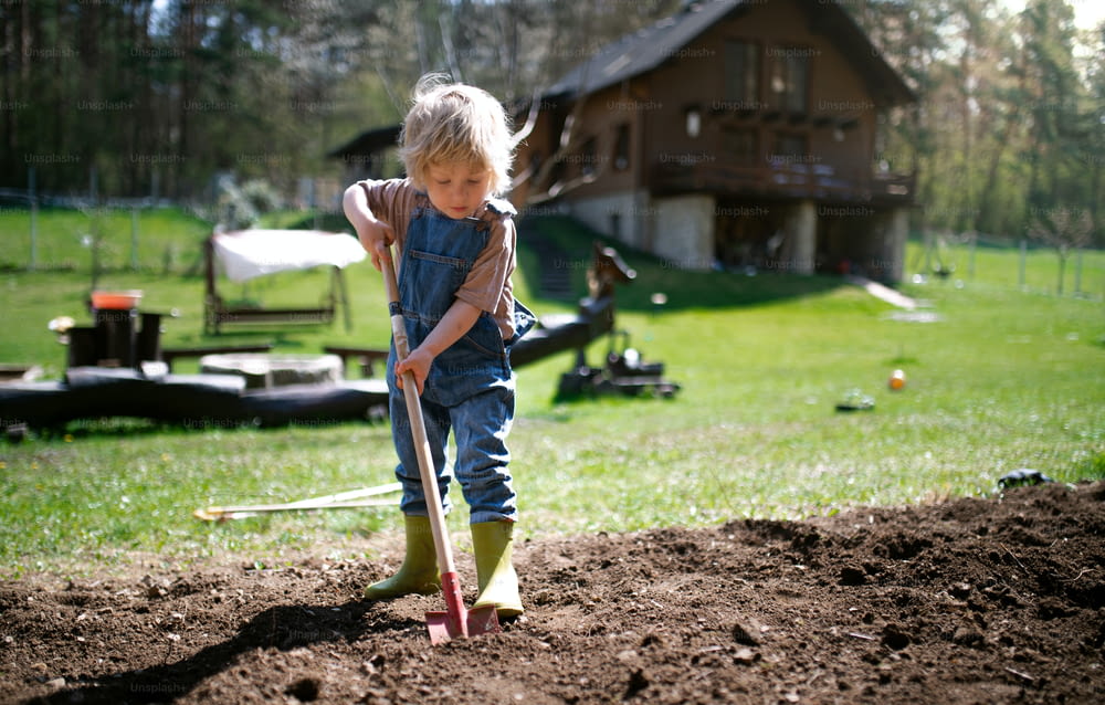 Glücklicher kleiner Junge, der draußen im Garten arbeitet, nachhaltiges Lifestyle-Konzept.