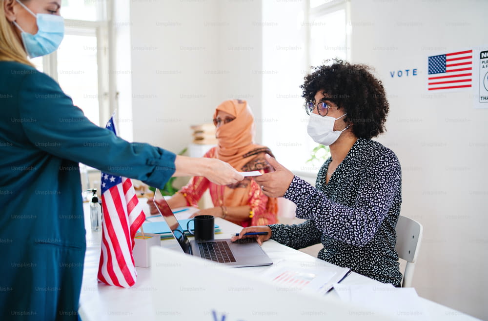Gruppe von Menschen mit Gesichtsmasken, die in Wahllokalen, US-Wahlen und Coronavirus wählen.
