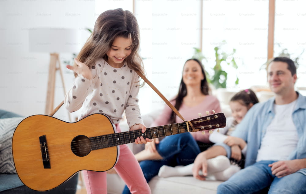 Portrait of small girl with family indoors at home, having fun with guitar.