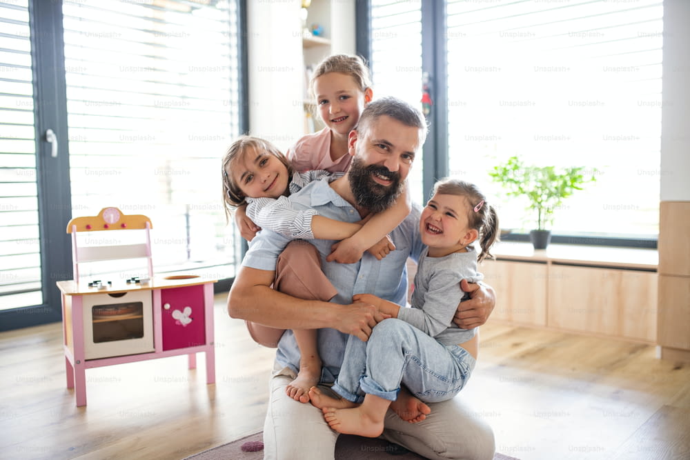 A father with three daughters indoors at home, looking at camera.