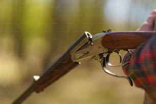 A close-up of hunter man charges the cartridge on rifle gun in forest.
