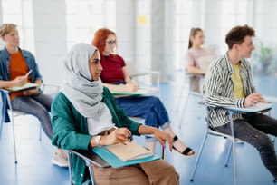 Un retrato de un grupo multiétnico de estudiantes universitarios sentados en el aula en el interior, estudiando.