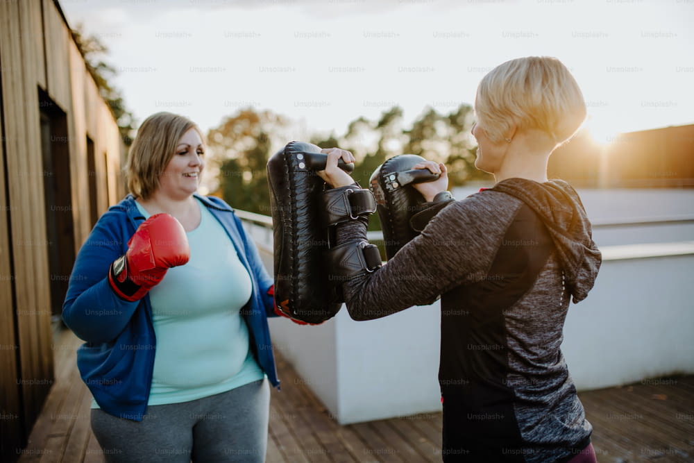Eine übergewichtige Frau trainiert Boxen mit Personal Trainer draußen auf der Terrasse.