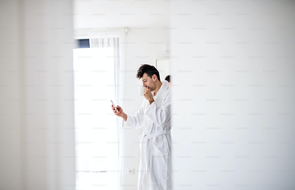 A young man with coffee and smartphone in the bedroom, a morning routine.
