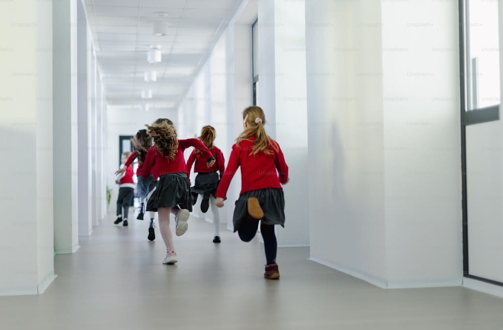 A rear view of schoolchildren in uniforms running in school corridor.