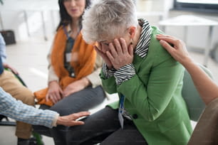 セラピーセッション中に輪になって座り、うつ病の女性を慰める高齢者のグループ。