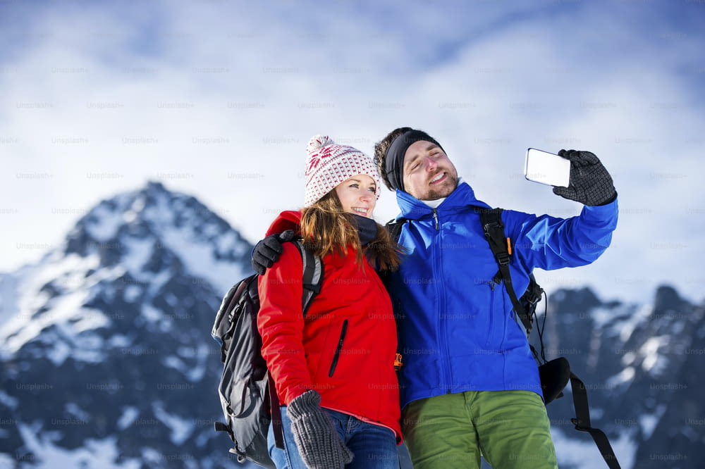 Junges Paar beim Selfie bei einer Wanderung draußen in sonnigen Winterbergen