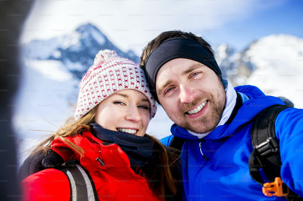 Junges Paar beim Selfie bei einer Wanderung draußen in sonnigen Winterbergen