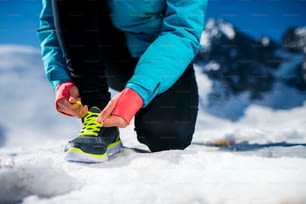 Joven corredora atándose los cordones de los zapatos al aire libre en la naturaleza invernal