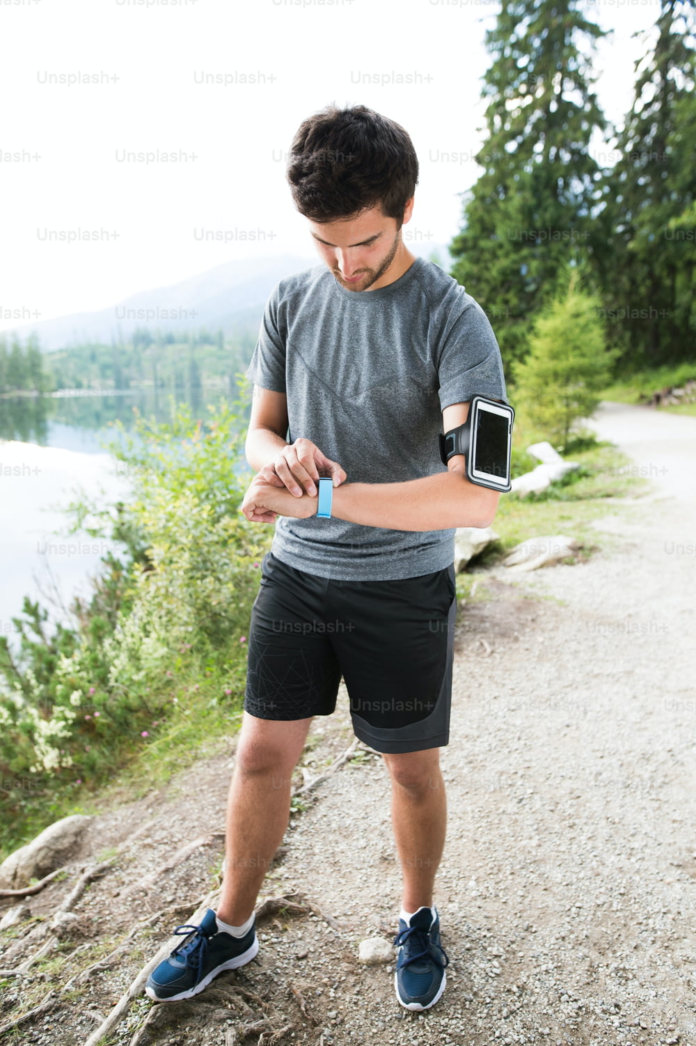 Young runner at the lake in green nature with smart phone and smartwatch. Using a fitness app for tracking weight loss progress, running goal or summary of his run.