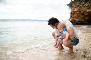 Jovem bonito segurando seu filho bebê na praia aproveitando o tempo à beira-mar.