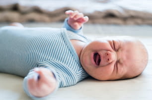 Cute newborn baby boy in blue striped onesie lying on bed, crying. Close up.