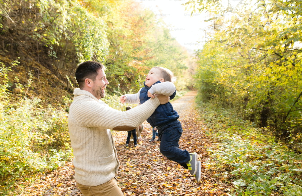 Father holding his little son, spinning him. Walk in colorful autumn forest.