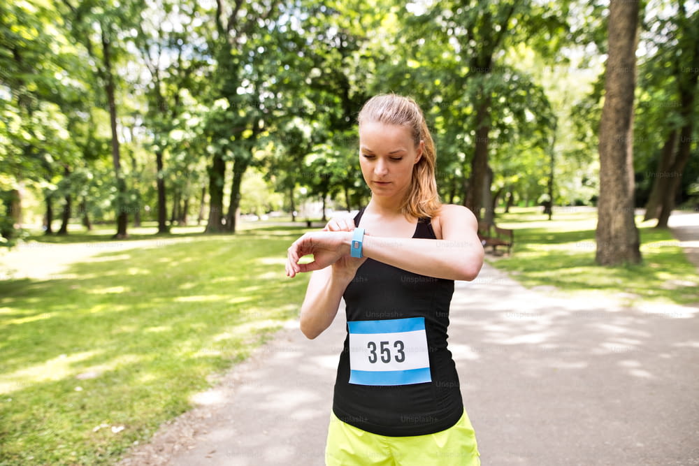Jeune femme mettant en place une montre avant d’aller courir dans un parc d’été vert et ensoleillé.