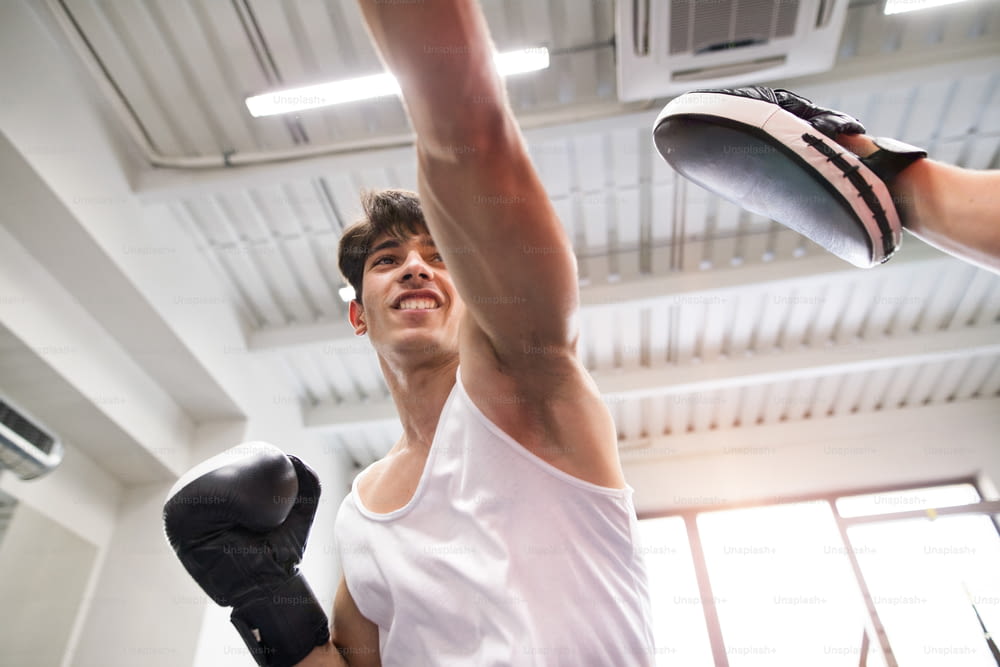 Handsome fit hispanic man in gym boxing with unrecognizable rival