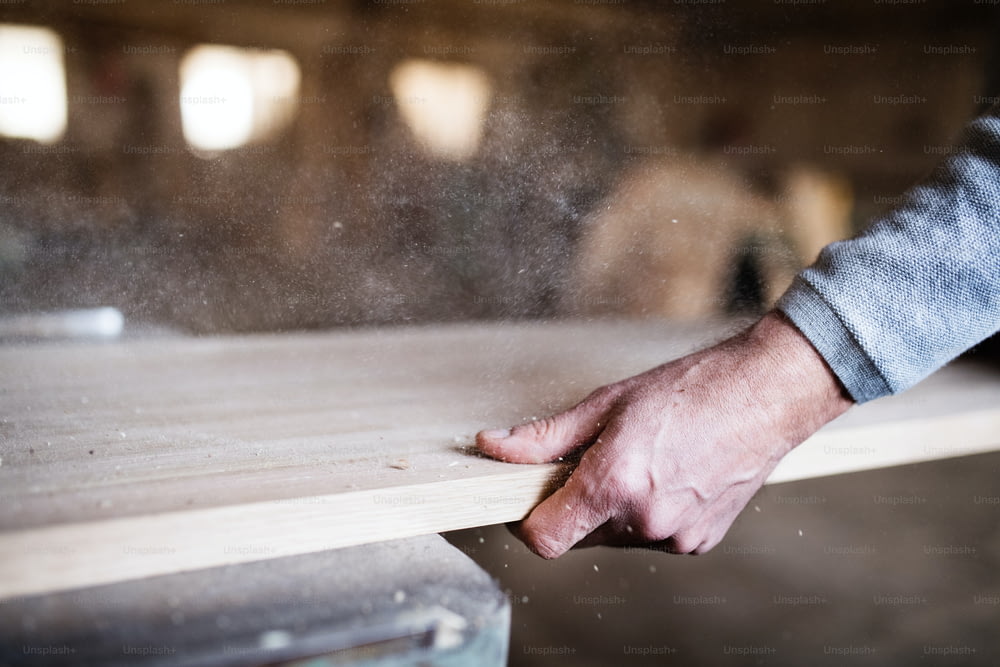 La main d’un ouvrier méconnaissable dans l’atelier de menuiserie, travaillant le bois.