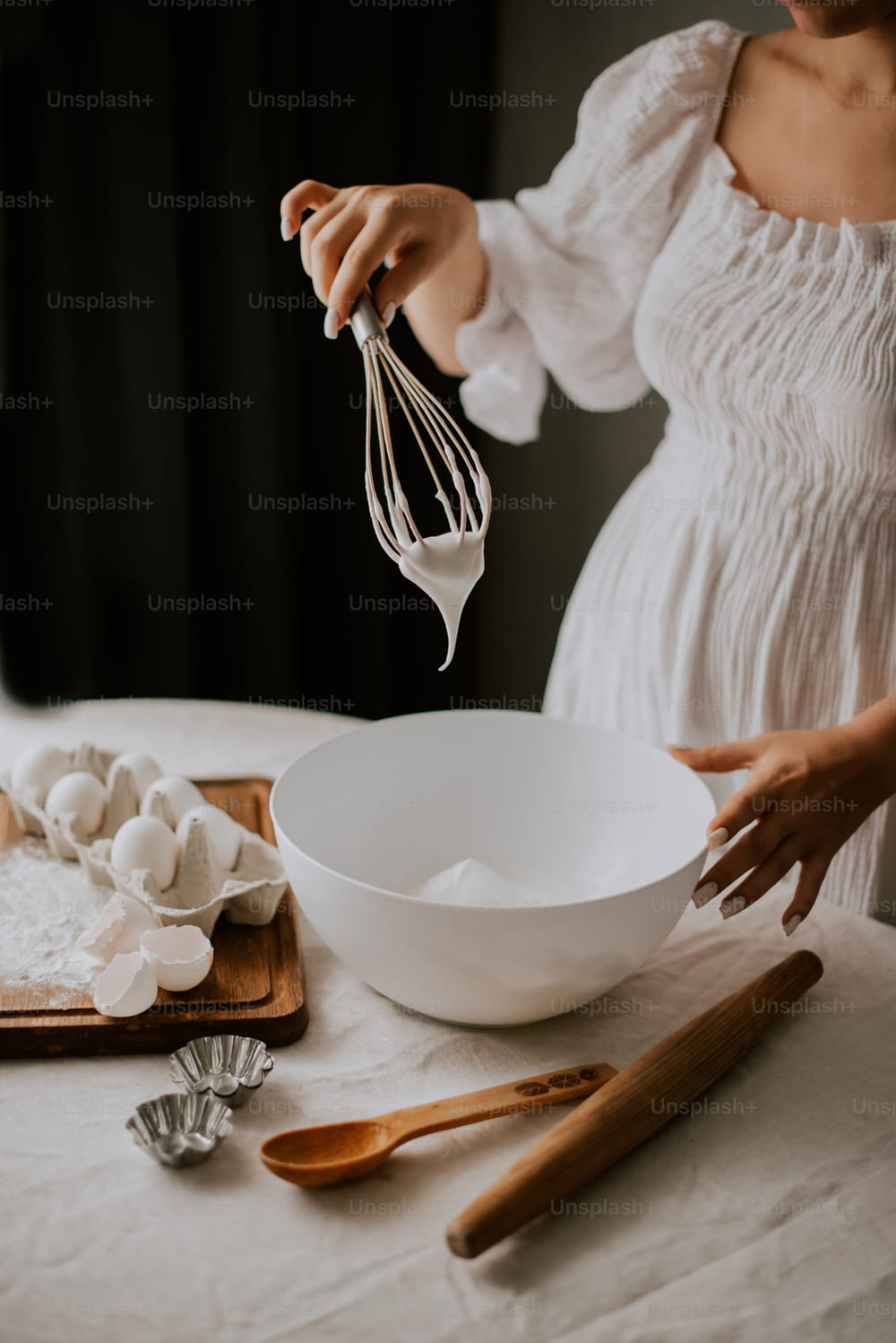 Uma mulher em um vestido branco bate ovos em uma tigela