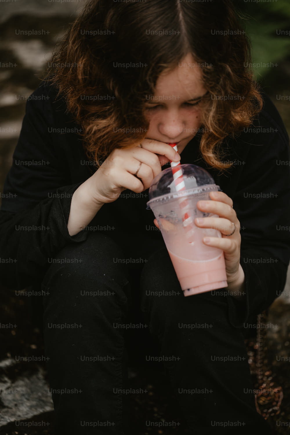 a woman sitting on the ground drinking from a pink cup