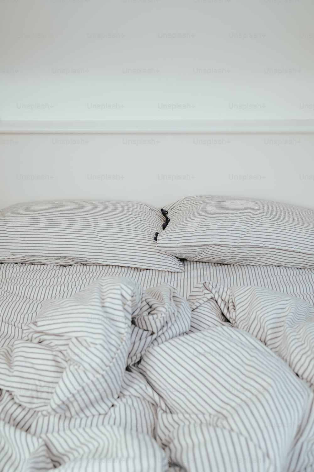 un lit défait avec une couette rayée et des oreillers