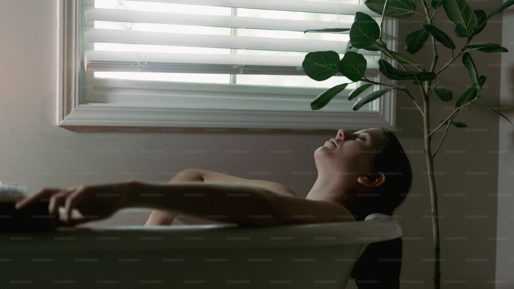 Una mujer acostada en una bañera junto a una ventana
