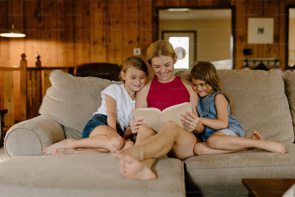 a woman and two girls sitting on a couch reading a book