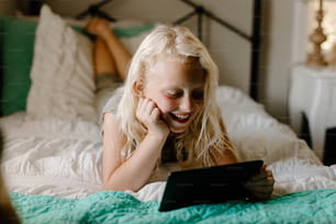 a little girl laying on a bed looking at a tablet