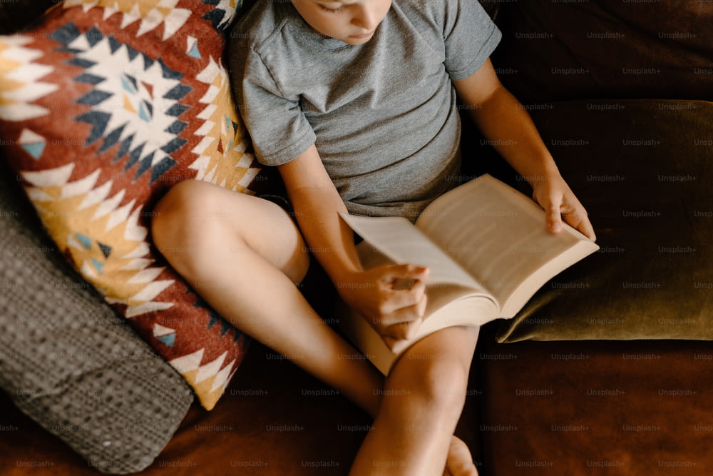 a young boy sitting on a couch reading a book