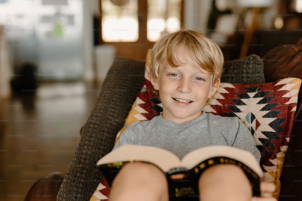 a young boy sitting in a chair holding a book