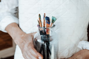 a person holding a jar filled with paint brushes