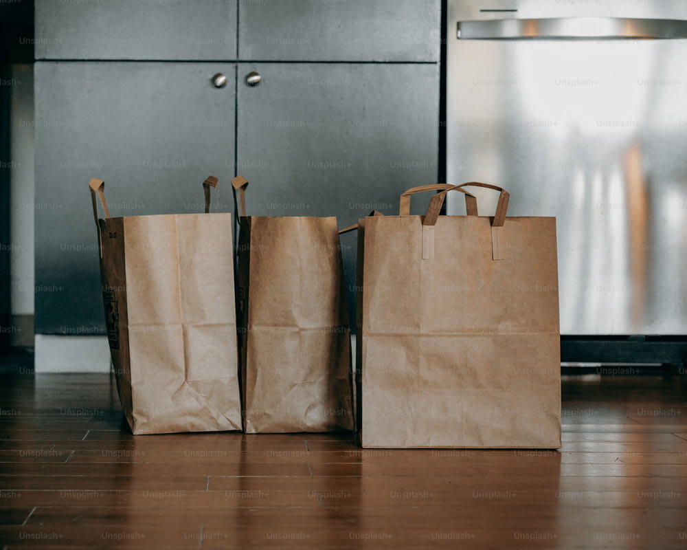 three brown paper bags sitting on top of a wooden floor