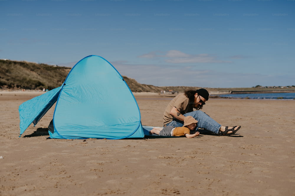 a man sitting on the beach next to a blue tent