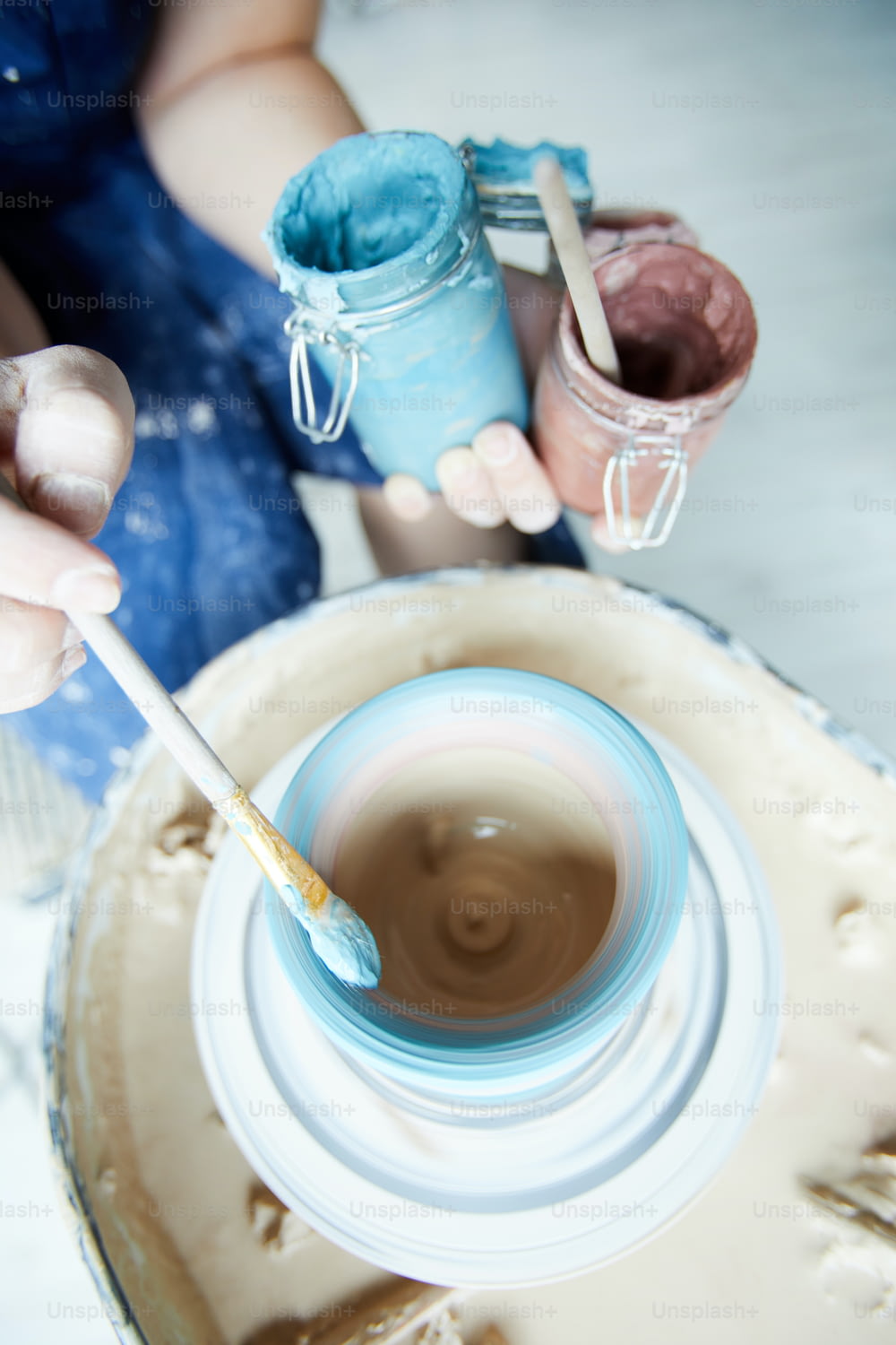 Paintbrush with blue color in hand of creative potter over rotating jug in pottery wheel