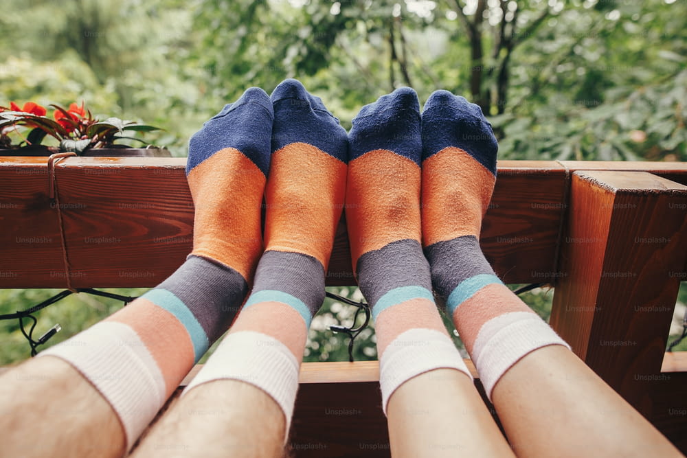 stylish hipster couple legs on wooden porch in colorful socks, in wooden cottage in forest in mountains. happy family relaxing together concept. summer vacation. funny moments