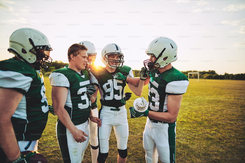Gruppo di giovani giocatori di football americano sorridenti in piedi insieme su un campo che tiene un trofeo del campionato