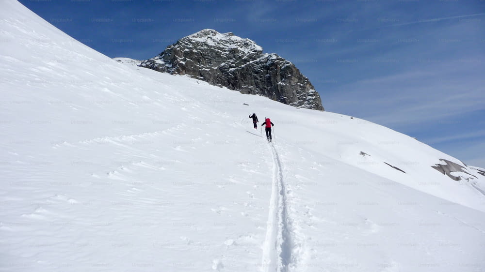 zwei Skitourengeher wandern im Winter unter blauem Himmel auf einen weit entfernten Berggipfel in den österreichischen Alpen