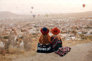 Les gens voyagent. Femmes En Chapeaux Assis Sur La Colline Appréciant Le Vol De Montgolfières Vue En Cappadoce En Turquie. Haute résolution