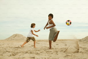 two children playing with a soccer ball in the sand