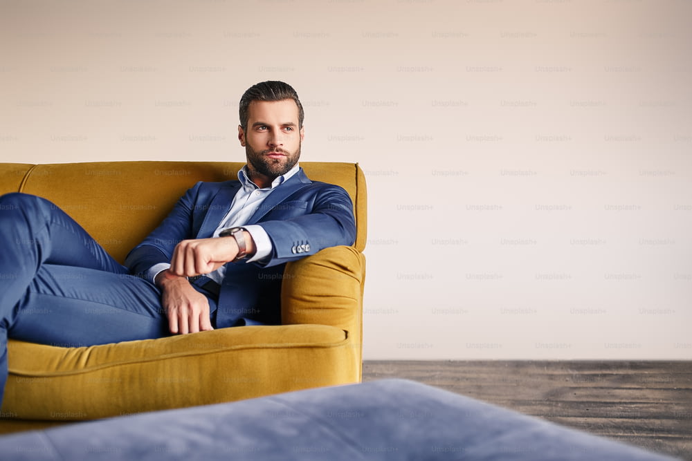 Sich entspannt fühlen... Ein gutaussehender und gut gekleideter Geschäftsmann ruht sich auf dem Sofa aus und denkt über Geschäfte nach. Mode-Look. Geschäftskonzept.