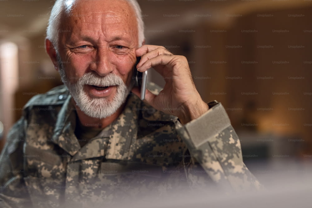 Soldado mayor sonriente usando el teléfono móvil y hablando con alguien en la oficina.