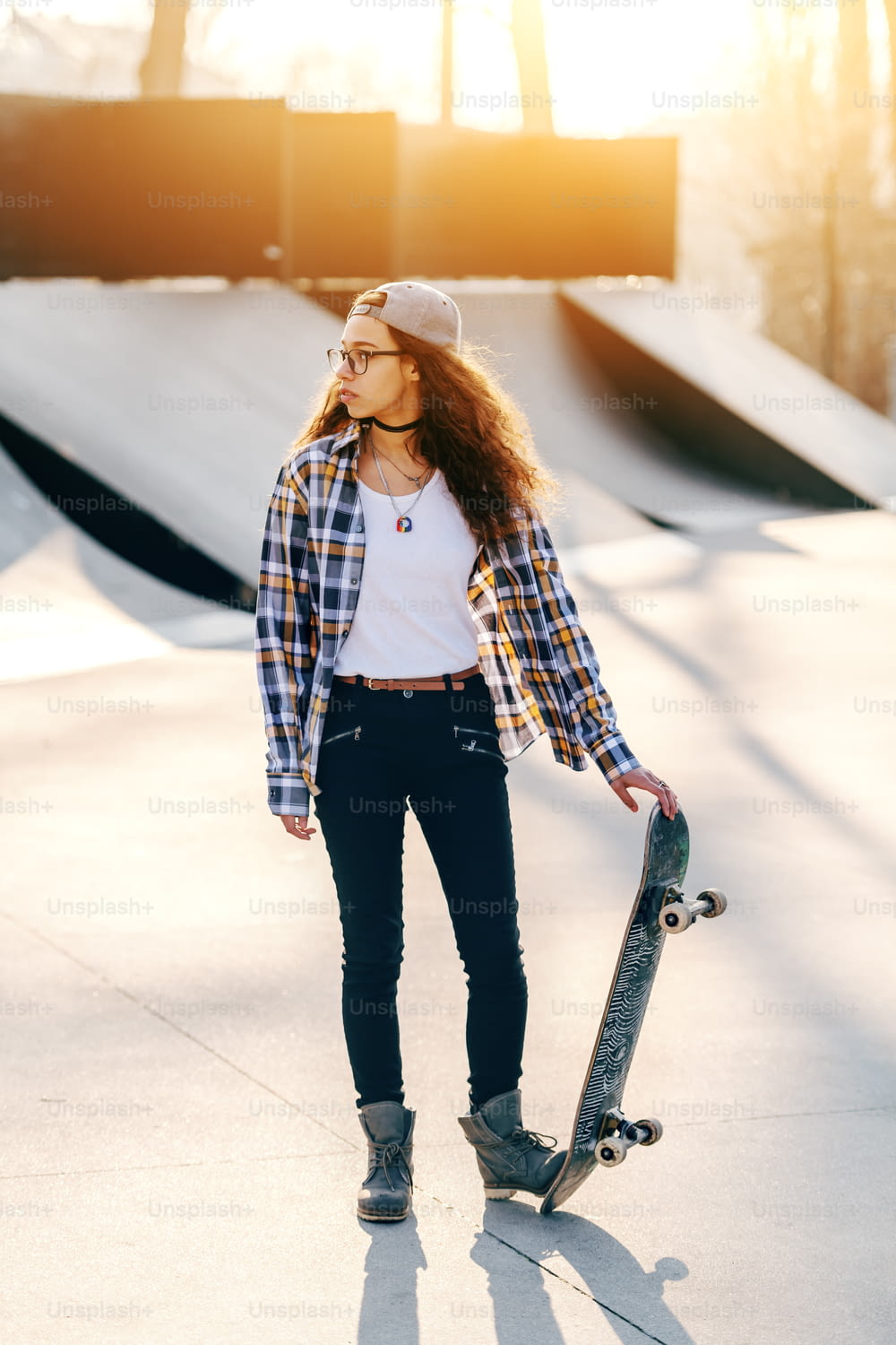 Beautiful mixed race teenage urban girl with curly hair posing with skateboard at skate park.