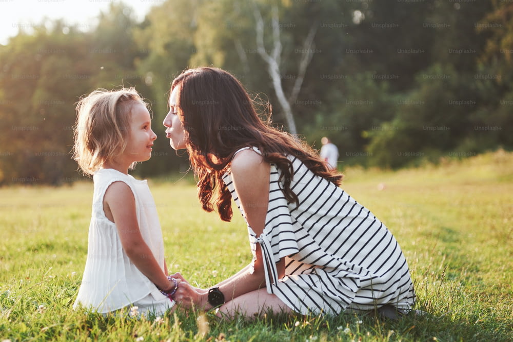 Mãe e filha felizes abraçando em um parque ao sol em um fundo brilhante de verão de ervas