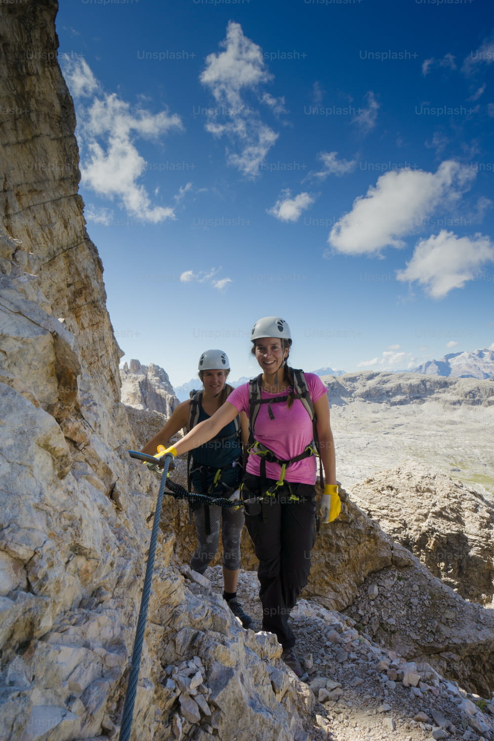 Vertical view of an attractive female climbers and twins on a steep Via Ferrata in the Italian Dolomites with a great view behind