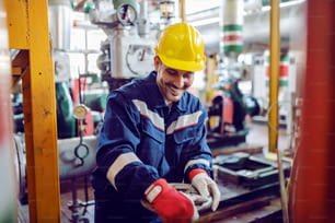 Smiling hardworking energy plant worker in working suit screwing valve.