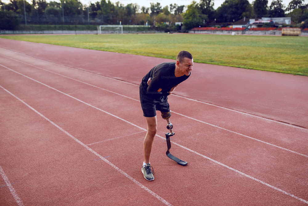 Sportlicher kaukasischer Mann mit künstlichem Bein, der auf der Laufbahn steht und Bauchschmerzen hat.
