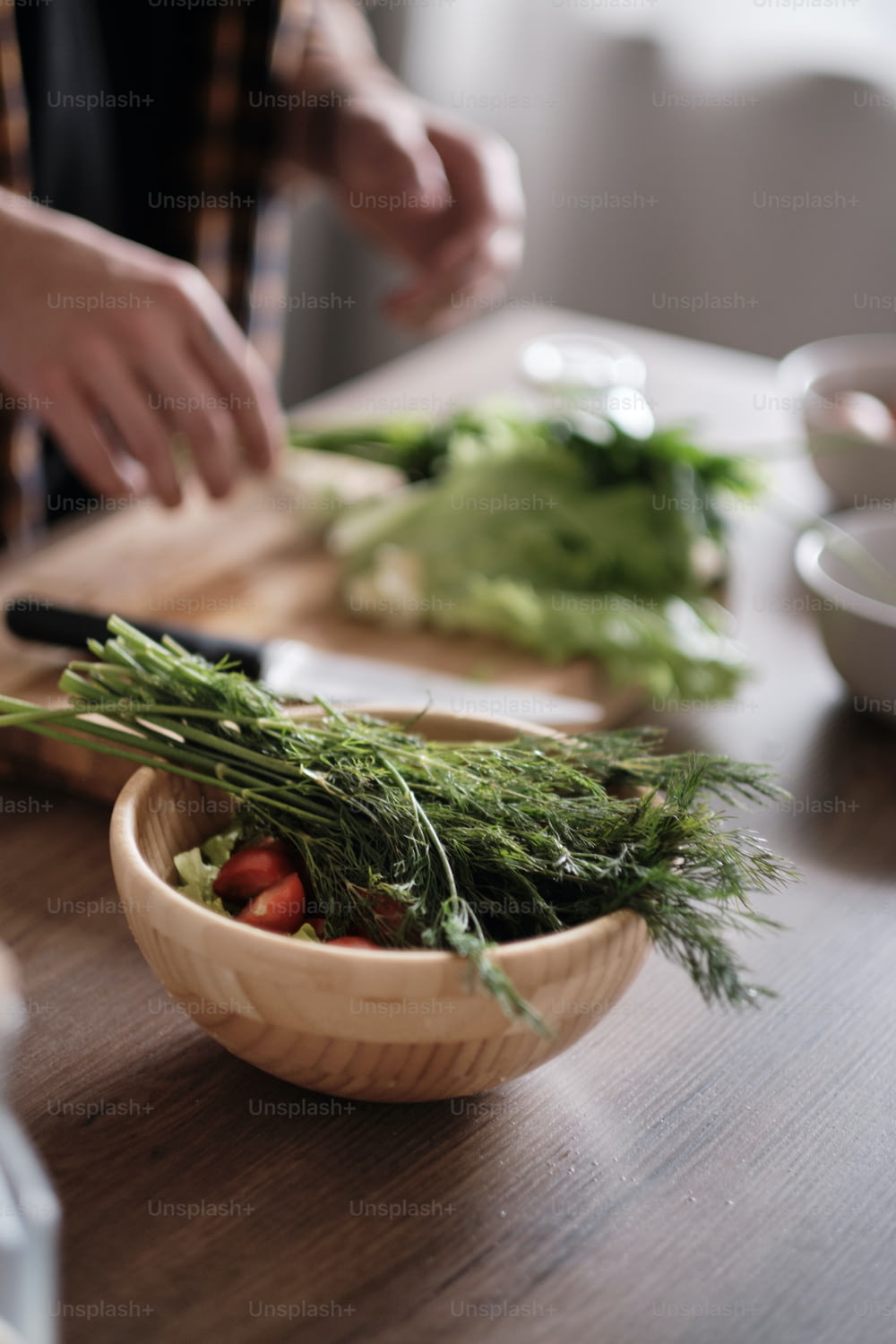 Primo piano delle mani dell'uomo che tagliano la lattuga verde in cucina, preparando l'insalata sul tavolo di legno