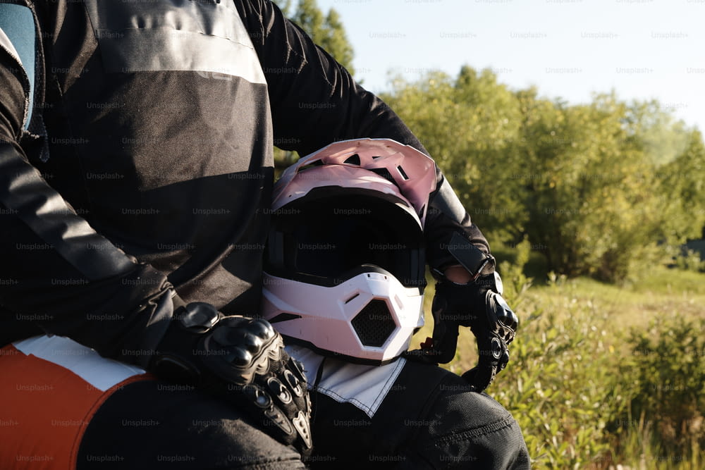 Close-up of unrecognizable motorcyclist in protective gloves sitting with helmet in forest