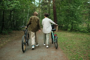 Rear view of young couple in casualwear talking to each other while moving down forest path or road between green trees
